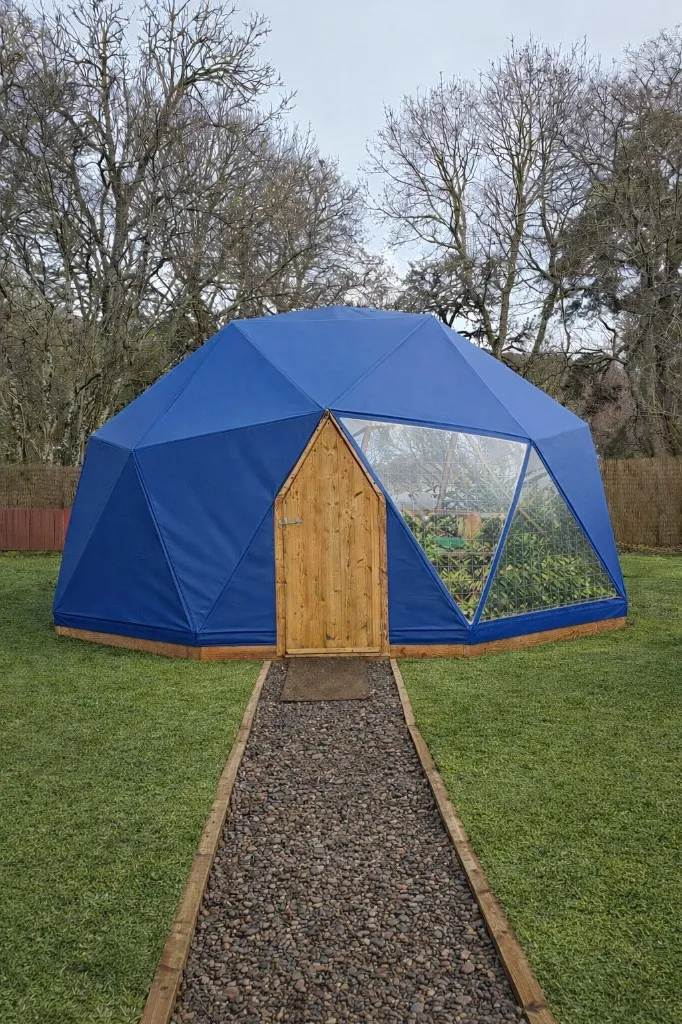 Super-insulated geodesic dome structure with blue weatherproof cover and integrated timber doorway by Highland Domes